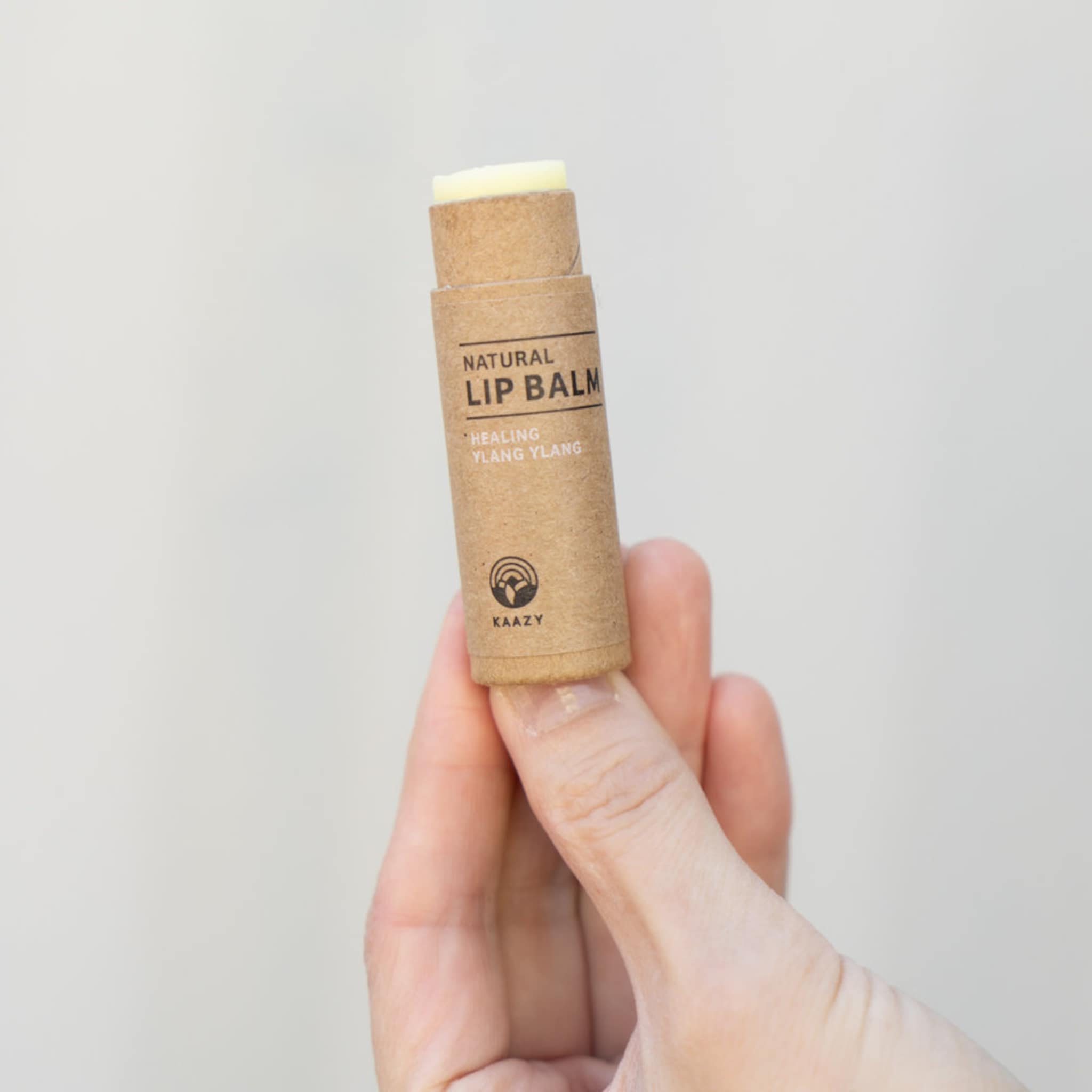 Lip balm tube in brown paper, white balm, held in hand, KAAZY brand visible
