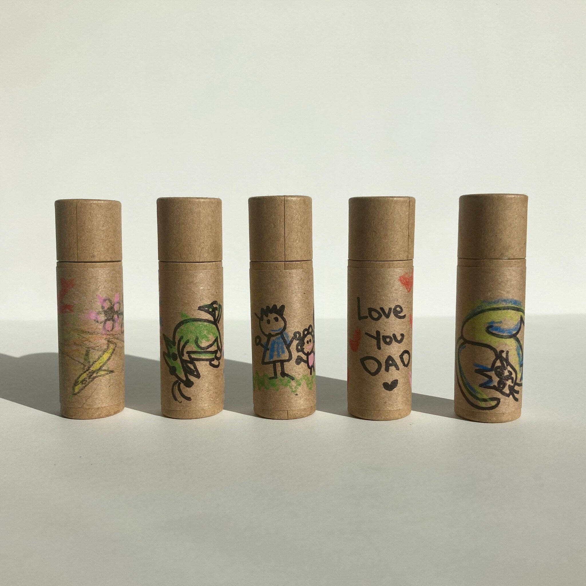 Lip balm tubes with brown paper material and colorful hand-drawn illustrations and text