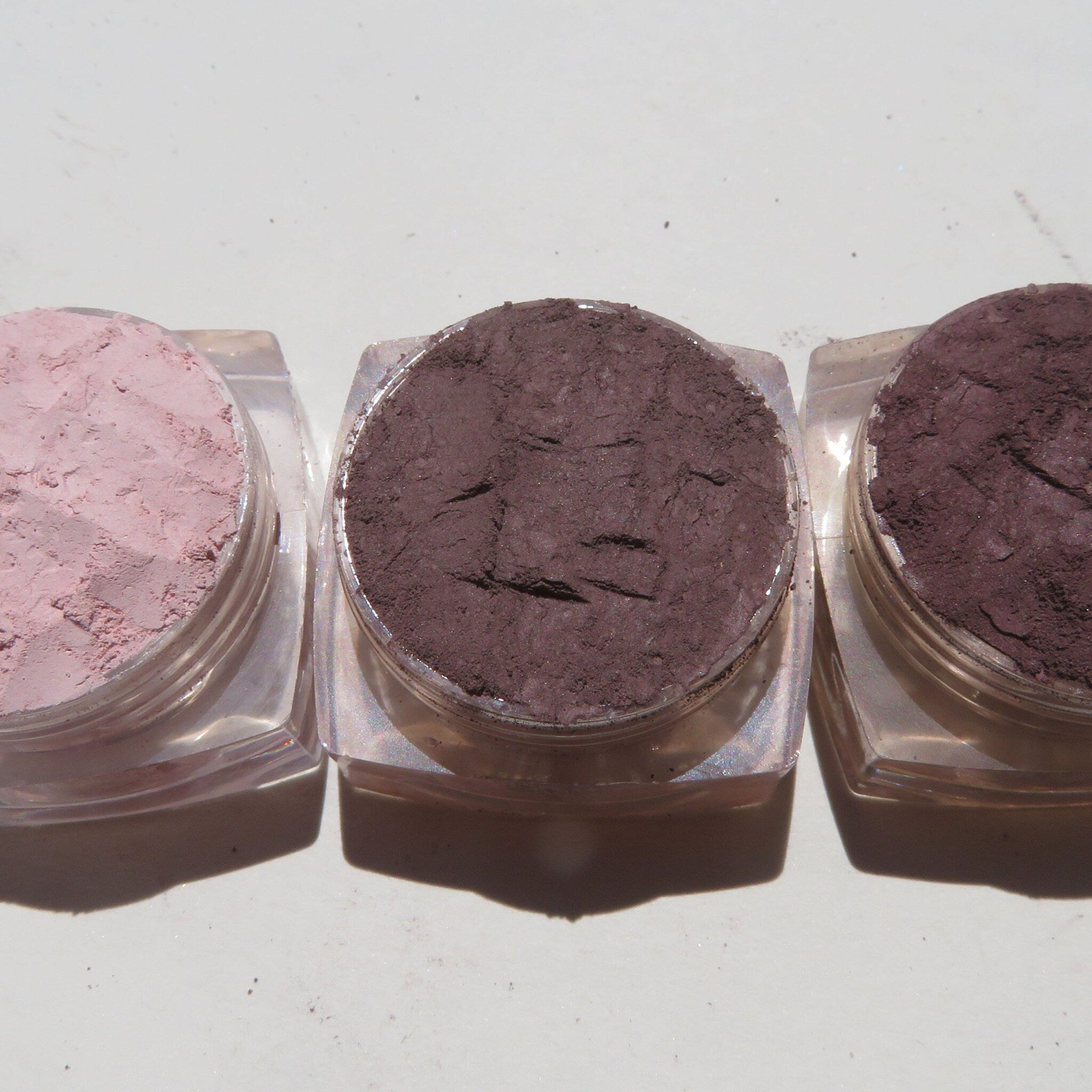 Close-up of three loose mineral eyeshadow pigments in matte neutral shades with vegan certification label visible
