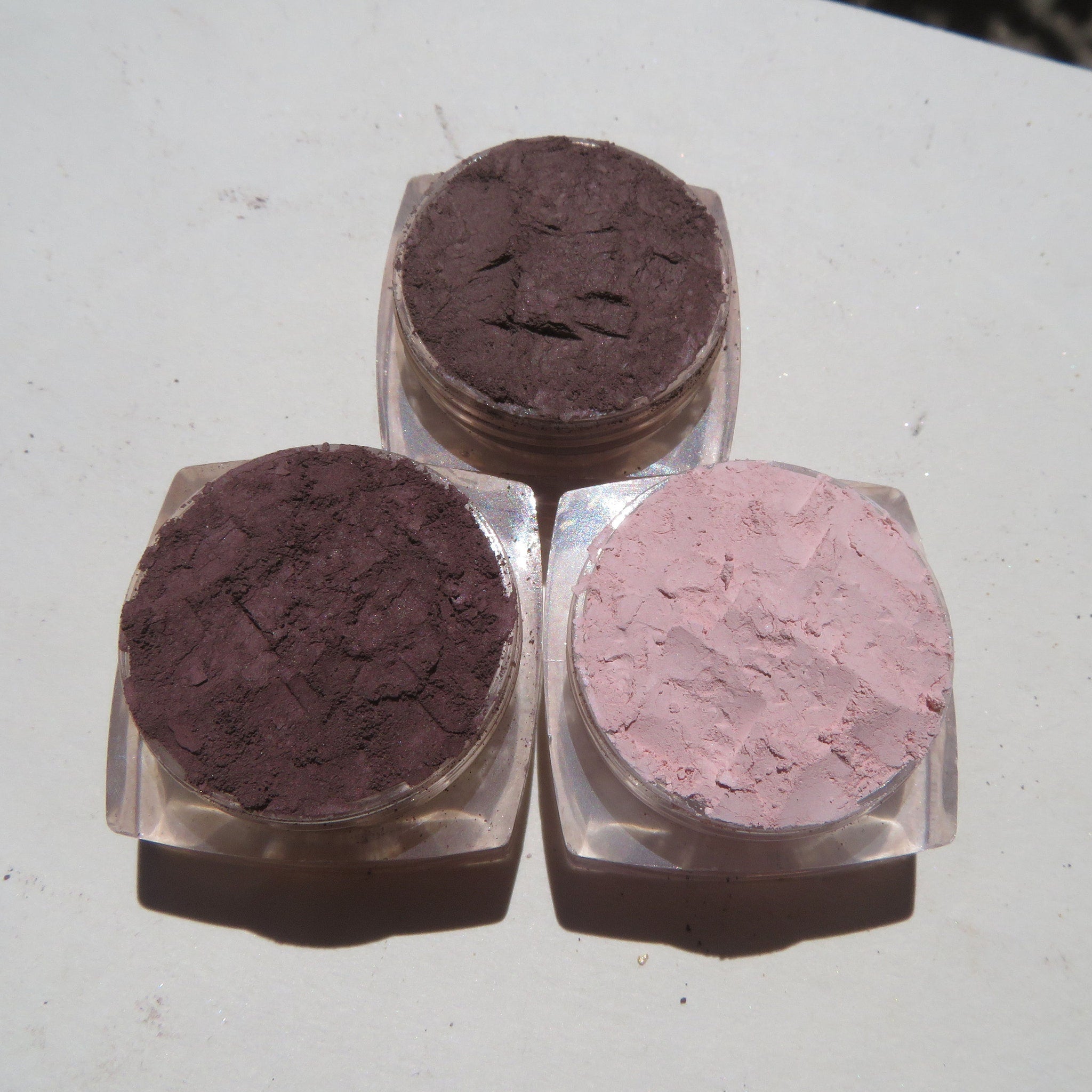 Three small jars of vegan matte mineral eyeshadow in neutral shades displayed on a marble surface with lids open.