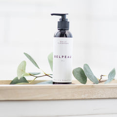 Daily cleanser bottle with black pump, white label, and Belpeau brand text on a wooden tray with greenery