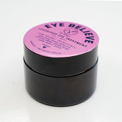 Eye treatment jar with pink label, black container, and "Eye Believe" text on label