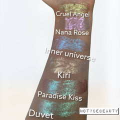 Close-up of three chameleon duochrome liquid eyeshadows in glass bottles with doe-foot applicators, showing shimmery violet, emerald, and bronze shades