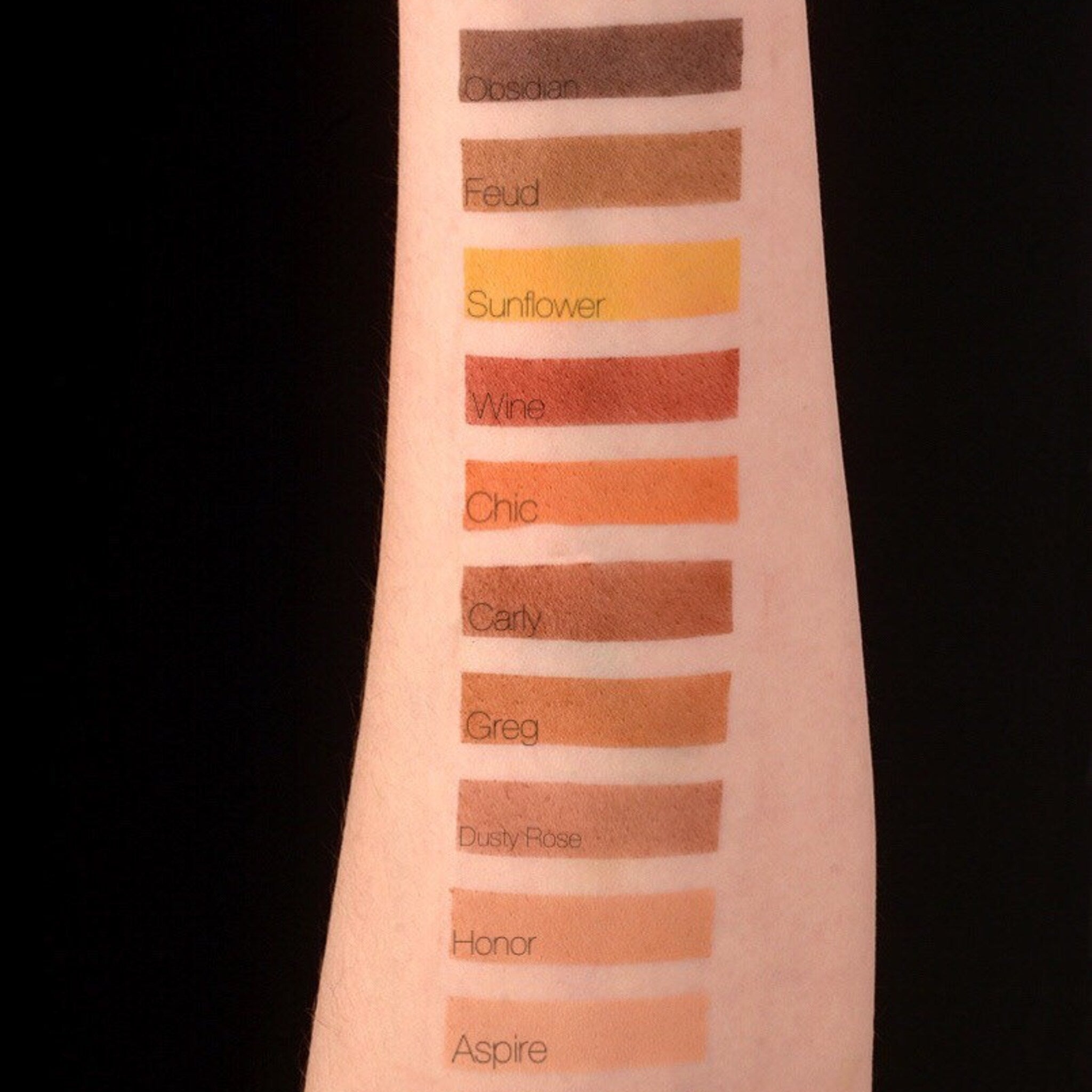 Swatches of eyeshadow colors in various shades on arm, including brown, yellow, and orange hues