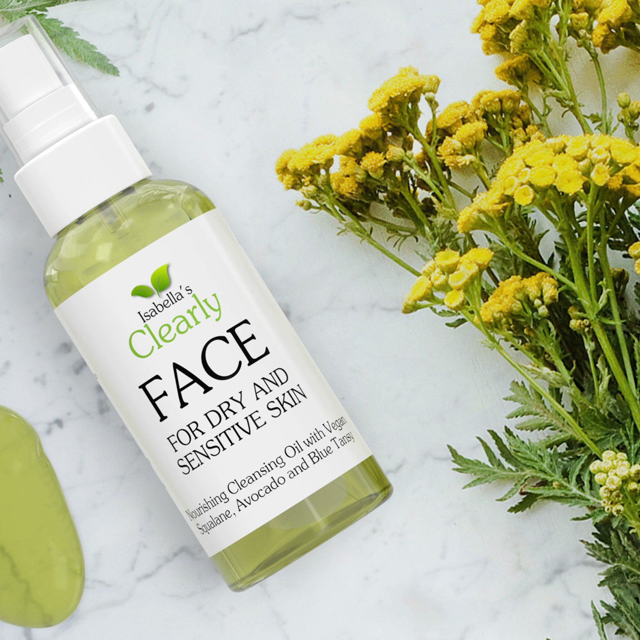 Face cleansing oil bottle with white label, green liquid, and yellow flowers on marble surface