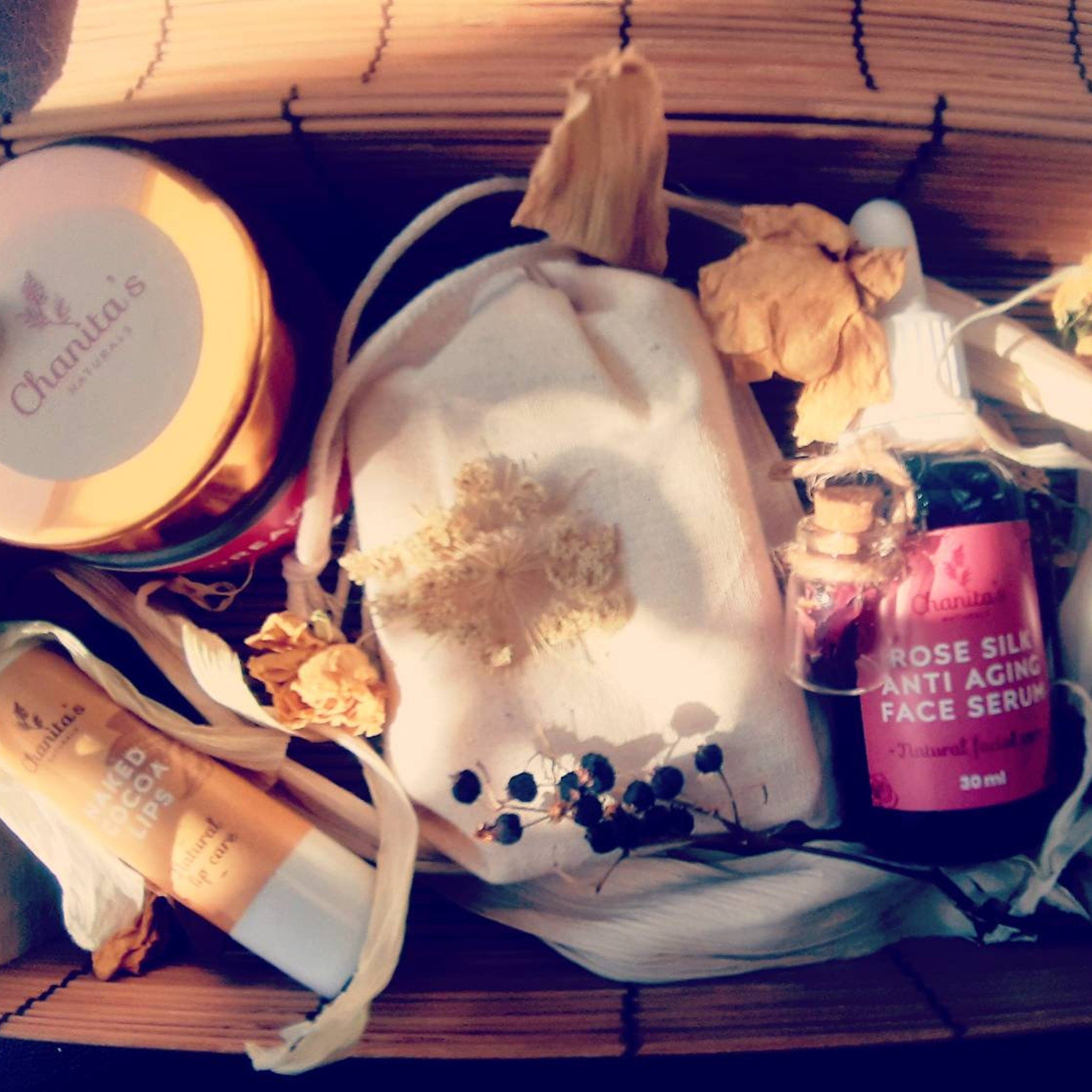 Skin care gift set with Chanita's Naturals products, wooden tray, white fabric, and dried flowers