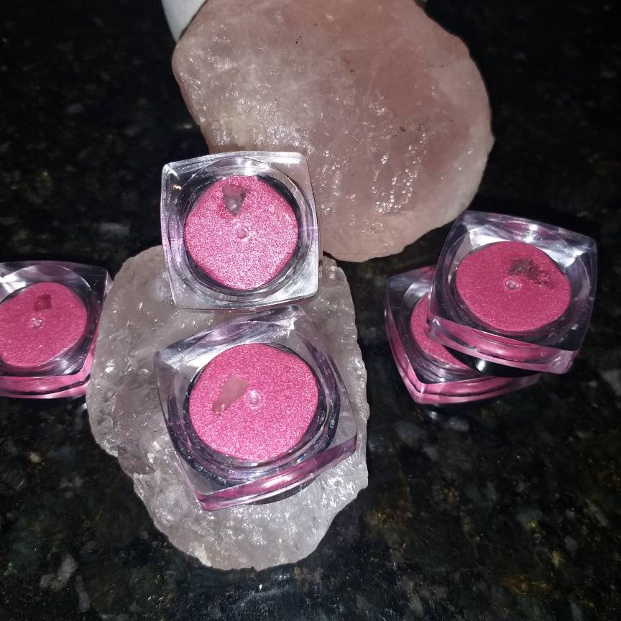 Pink eyeshadow pots with glittery finish in clear plastic containers on a rock formation