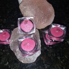 Pink eyeshadow pots with glittery finish in clear plastic containers on a rock formation