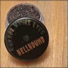 Side view of Hellhound loose eye shadow pigments in a sleek black jar with silver lid, showcasing fine shimmer particles.