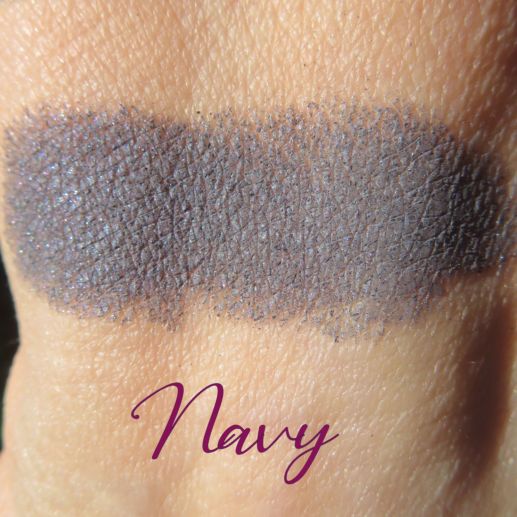 Close-up of navy blue shimmer loose powder eyeshadow with reflective particles in a clear sifter jar