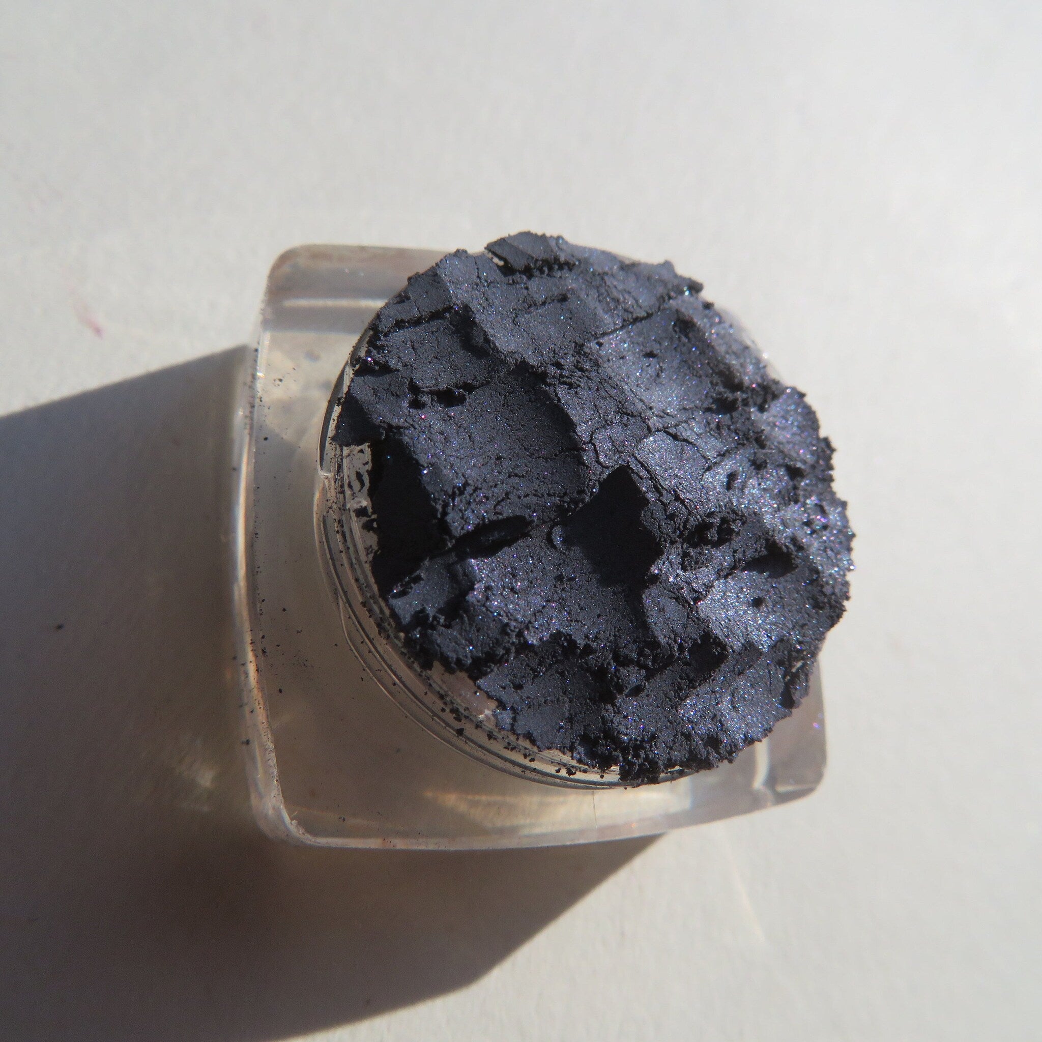 Open jar of navy blue shimmer loose powder eyeshadow with soft brush on marble surface