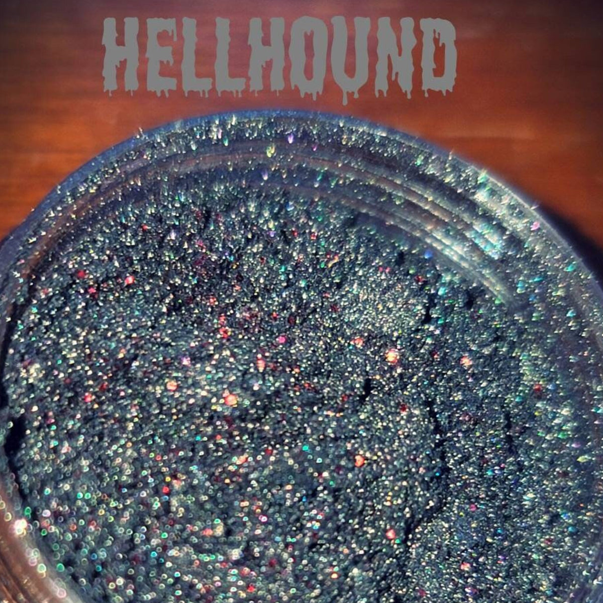 Close-up of Hellhound loose eye shadow pigment in a sleek black jar with silver lid, showcasing vibrant color payoff