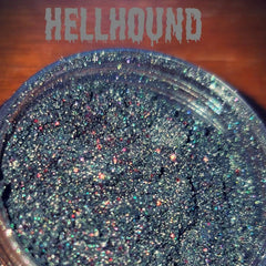 Close-up of Hellhound loose eye shadow pigment in a sleek black jar with silver lid, showcasing vibrant color payoff