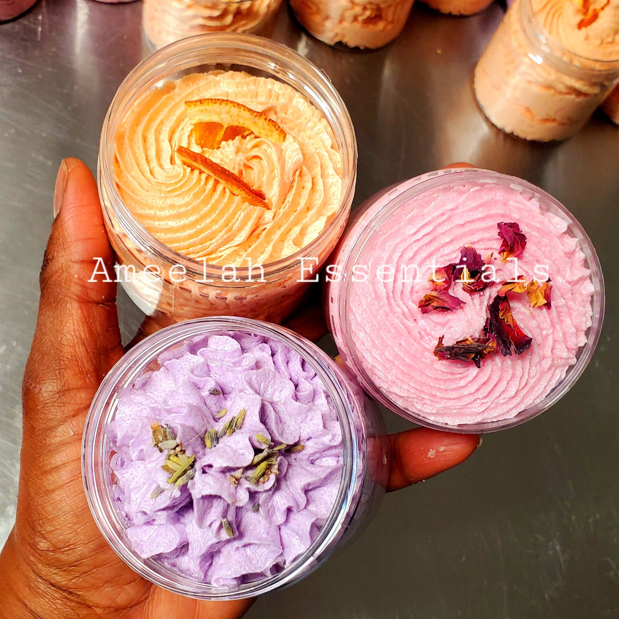 Whipped body butter, orange, pink, and purple, swirled texture, topped with dried herbs, Ameelah Essentials
