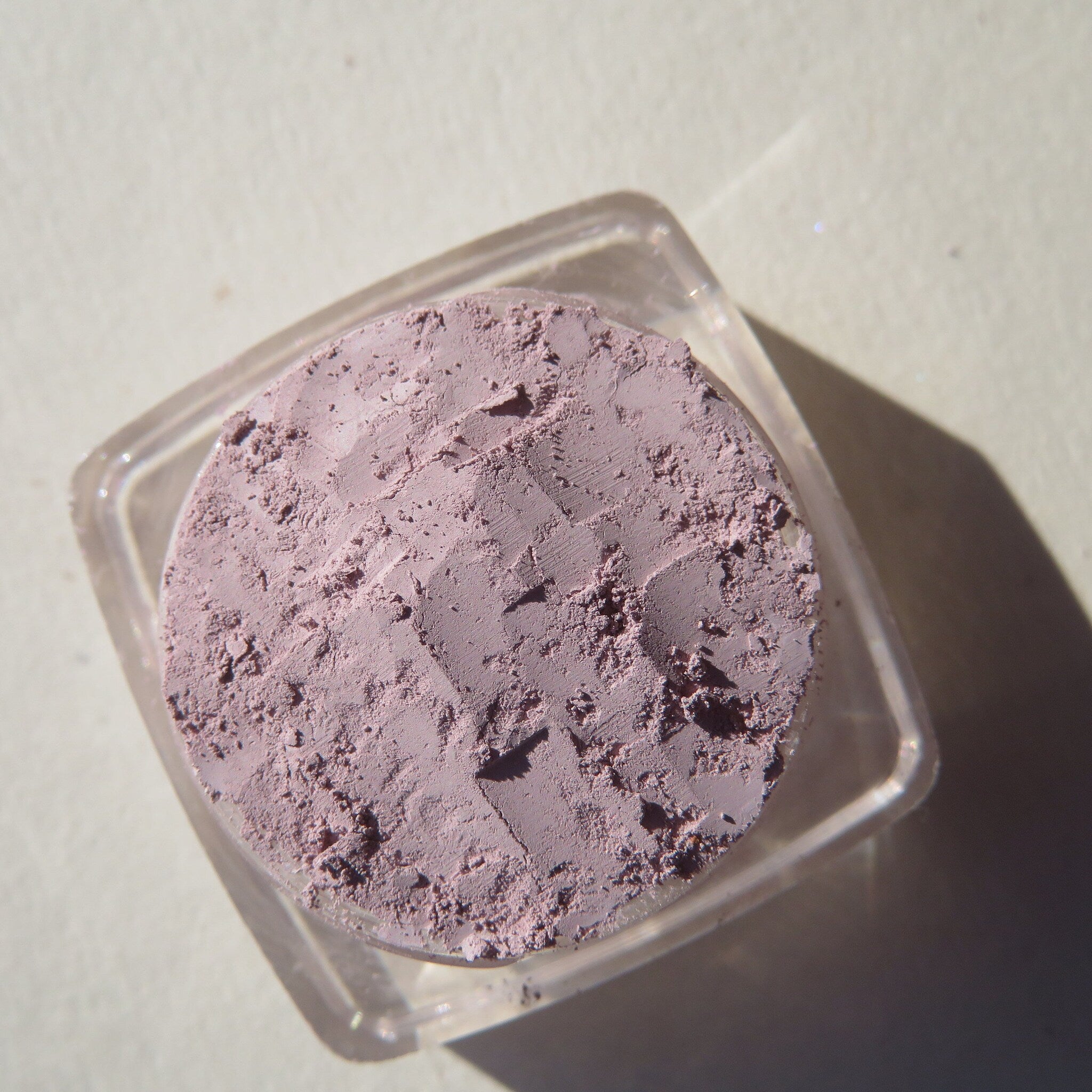 Side view of muted pale purple matte mineral eyeshadow in loose powder form, showing texture and vegan cruelty-free packaging