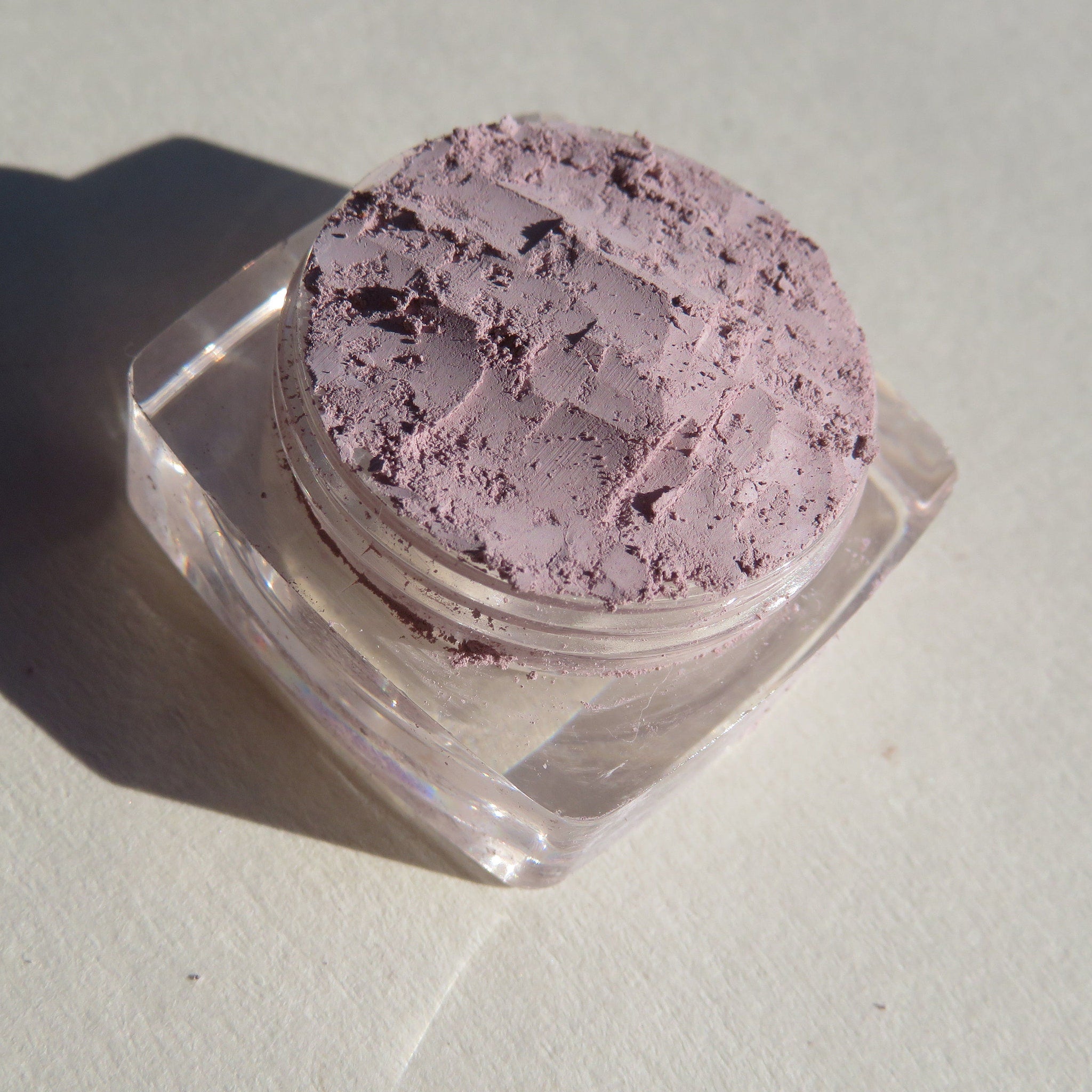 Side view of loose mineral eyeshadow in muted pale purple matte finish, showcasing fine powder texture
