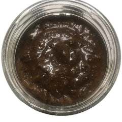 Brown paste in a clear glass jar with a glossy, textured surface and a reflective glass rim