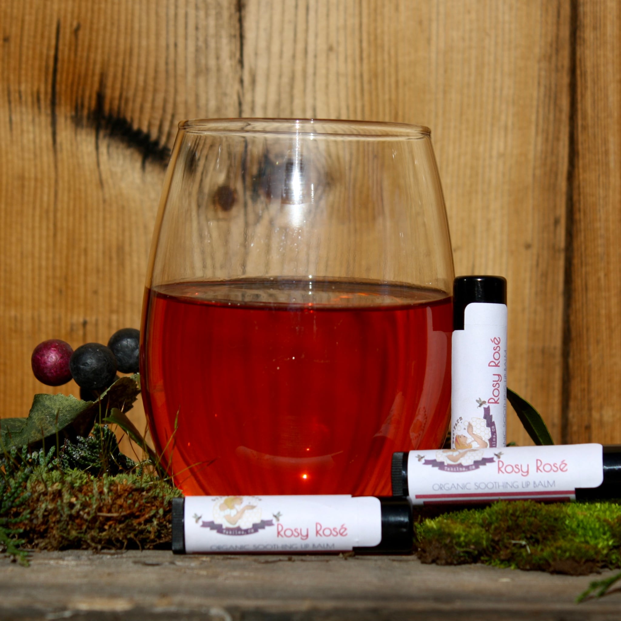 Lip balm tubes with white labels, black caps, and Rosy Rosé branding on moss