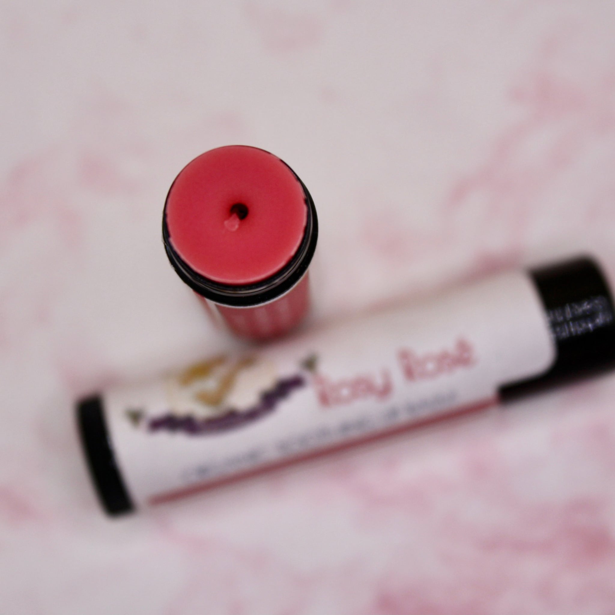 Lip balm with red color, black tube, and "Rosy Rose" text on label