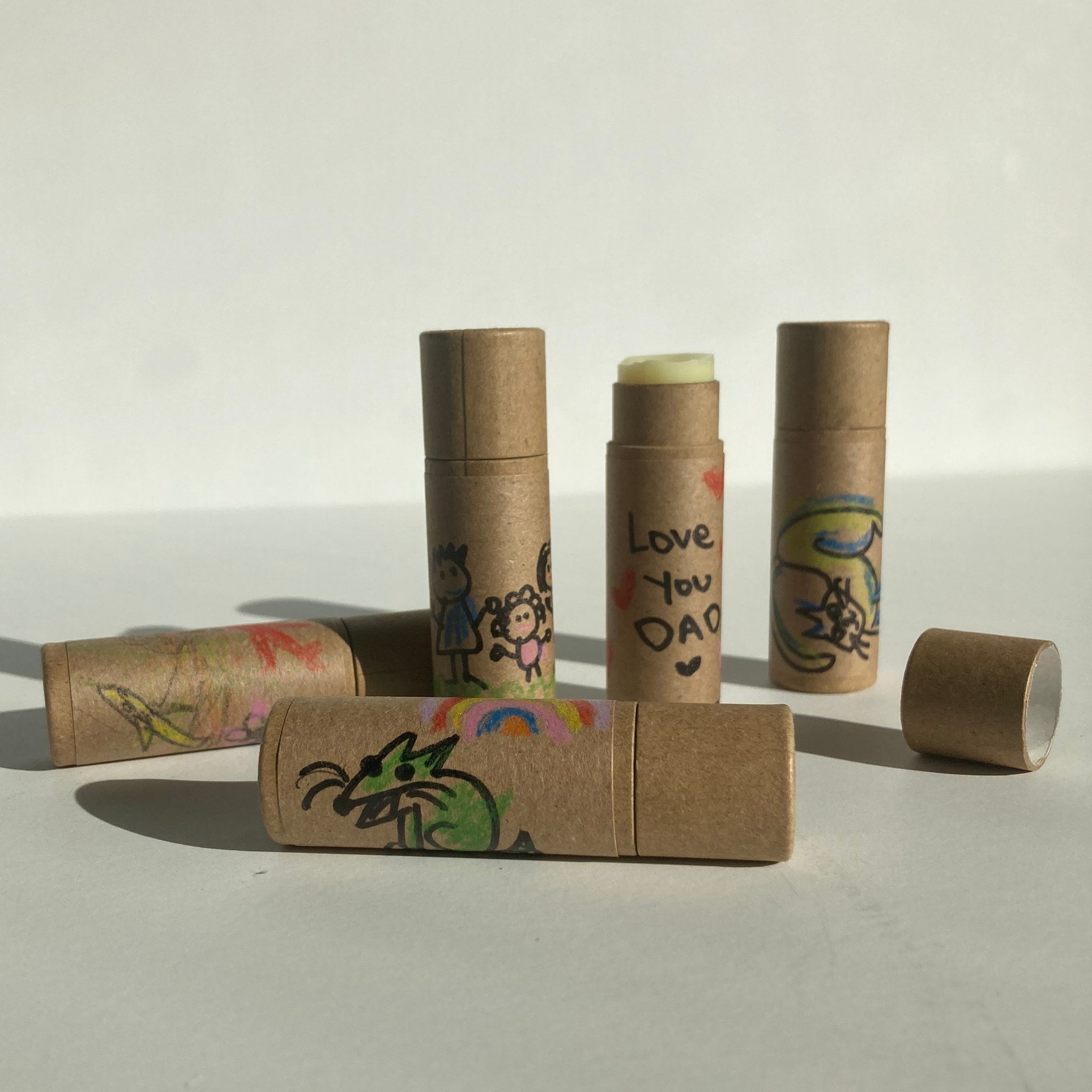 Lip balms in brown cardboard tubes with colorful drawings and text, one open showing balm