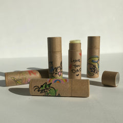 Lip balms in brown cardboard tubes with colorful drawings and text, one open showing balm