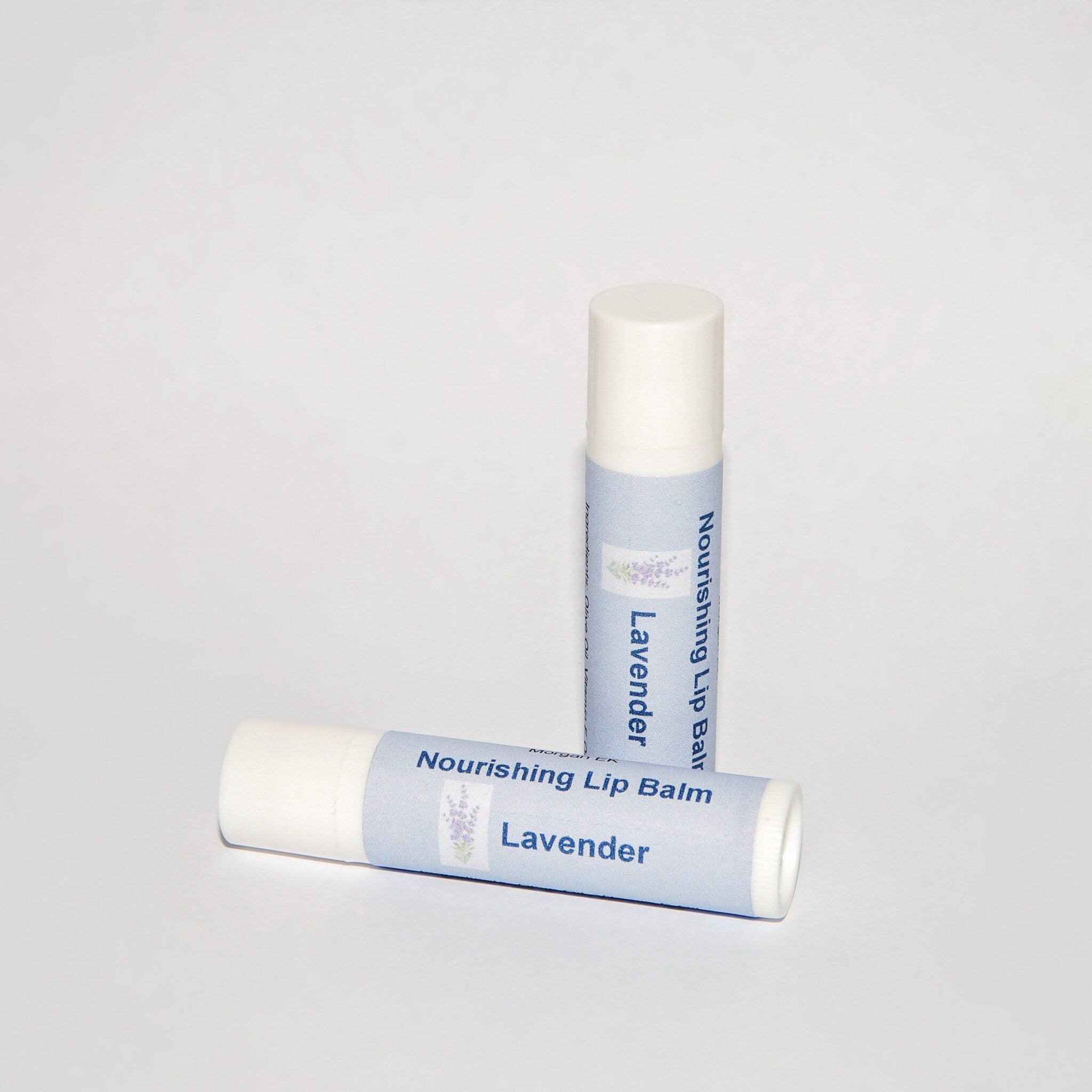 Lip balm tubes with white and light blue labels, MorganEK branding, and lavender text