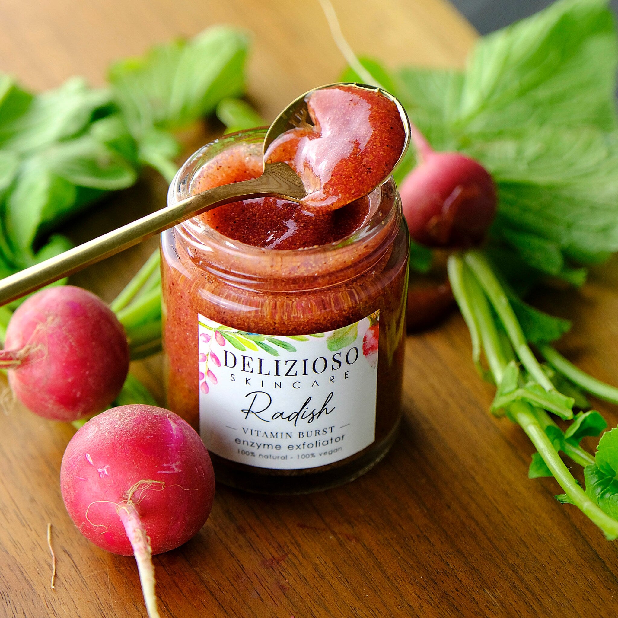 Radish enzyme exfoliator in glass jar with golden spoon, red and green produce, Delizioso Skincare label