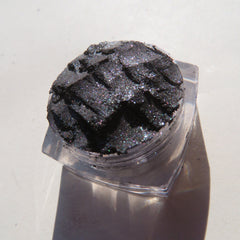Close-up of loose black silver shimmer eyeshadow pigment with metallic sheen in a small jar