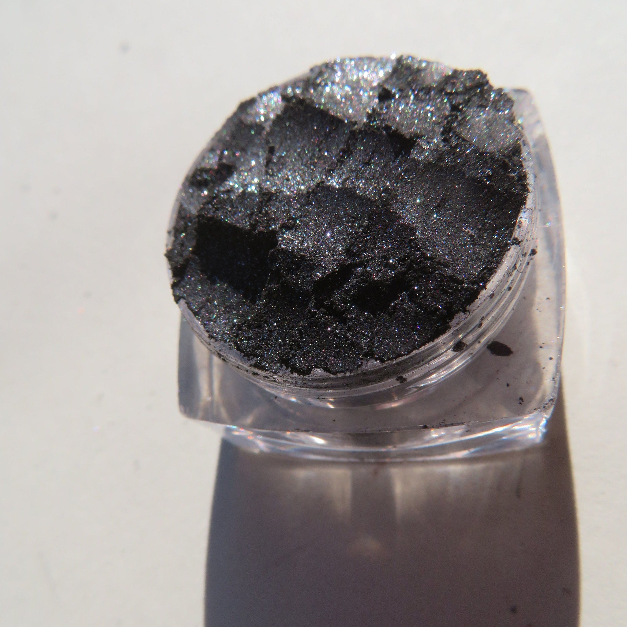 Close-up of loose black silver shimmer eyeshadow pigment with mineral sparkle in a small jar