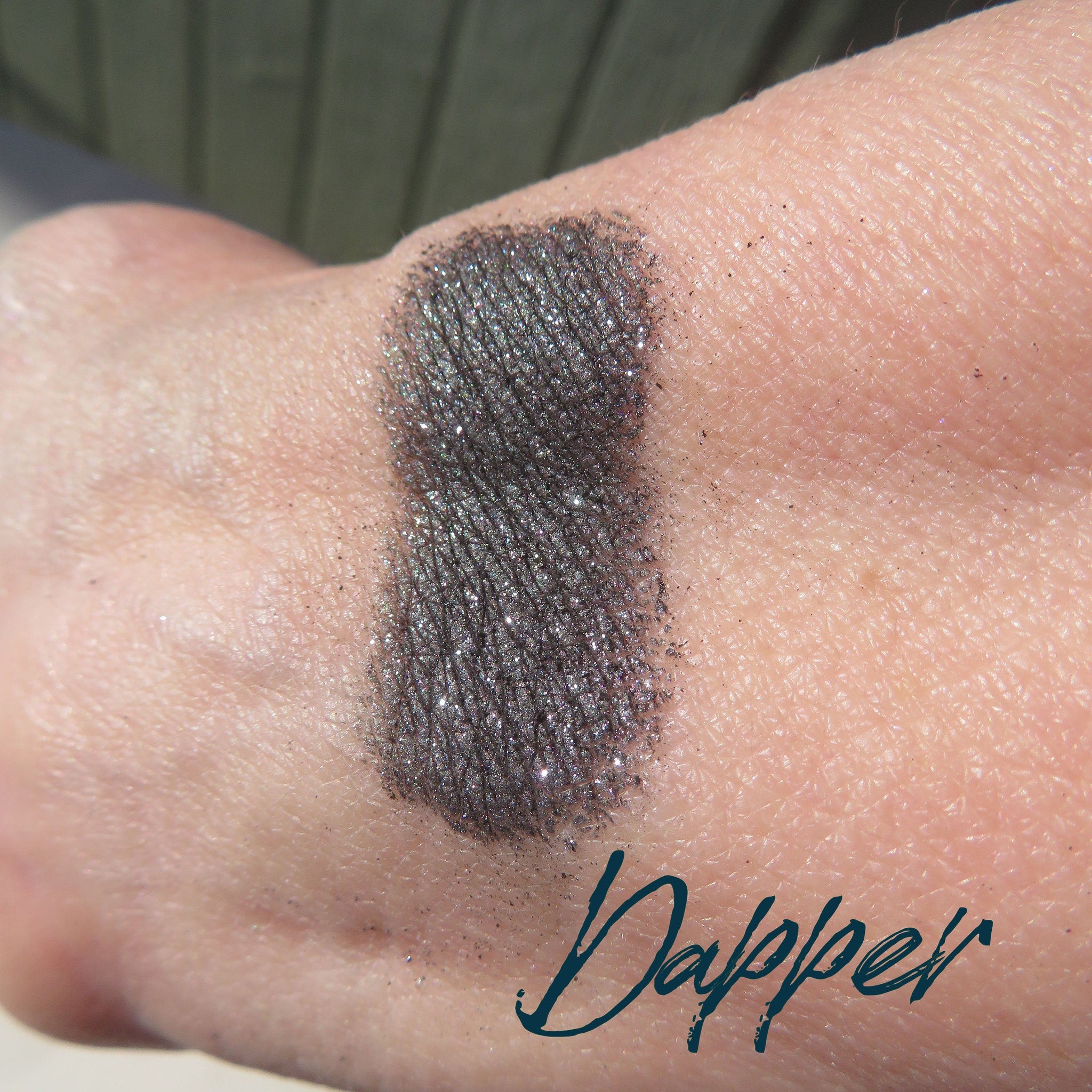 Side view of loose black silver shimmer eyeshadow powder spilling from jar onto marble surface