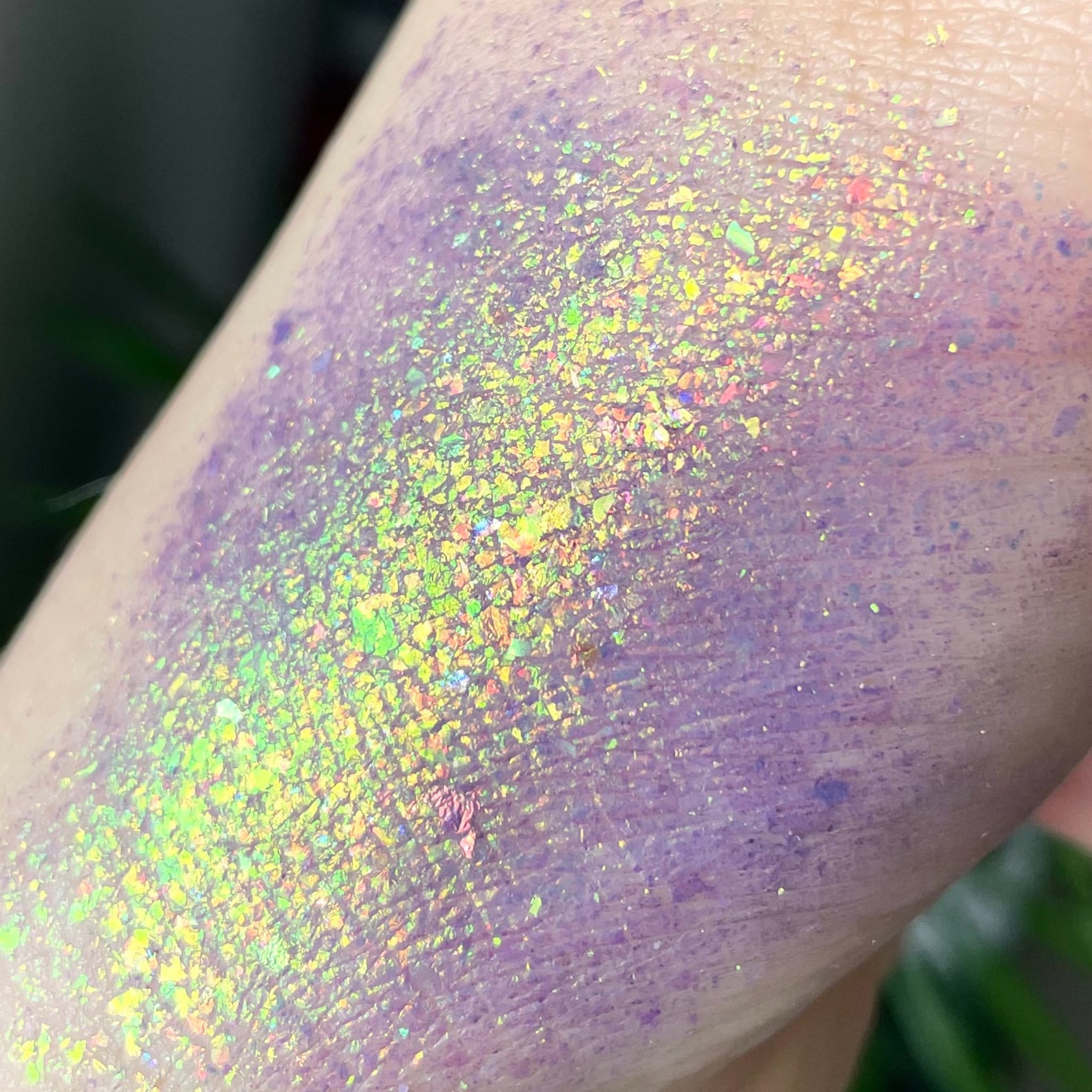 Purple glitter eyeshadow swatch with iridescent flakes on skin, close-up view