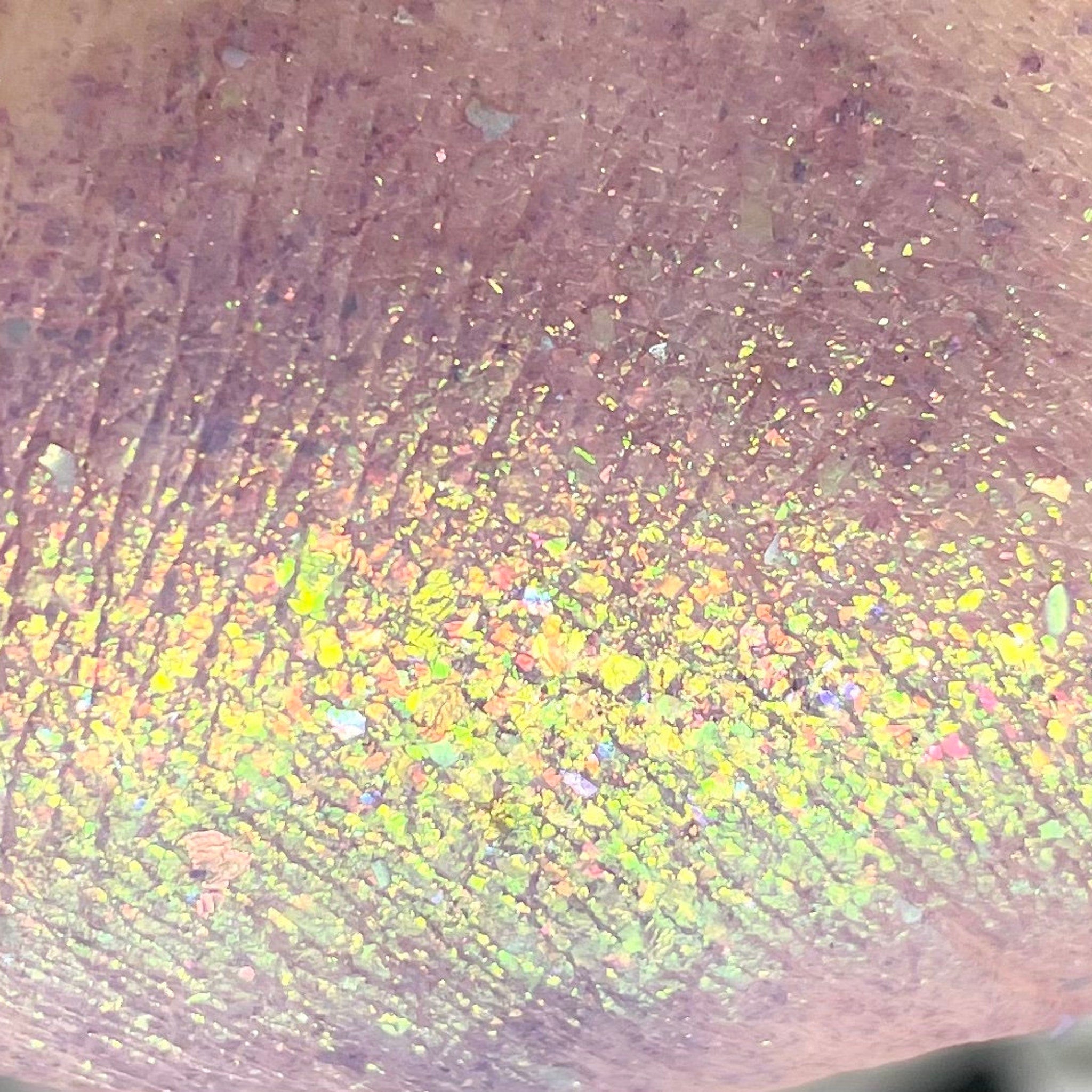 Glitter flakes with iridescent yellow and pink hues on a textured surface