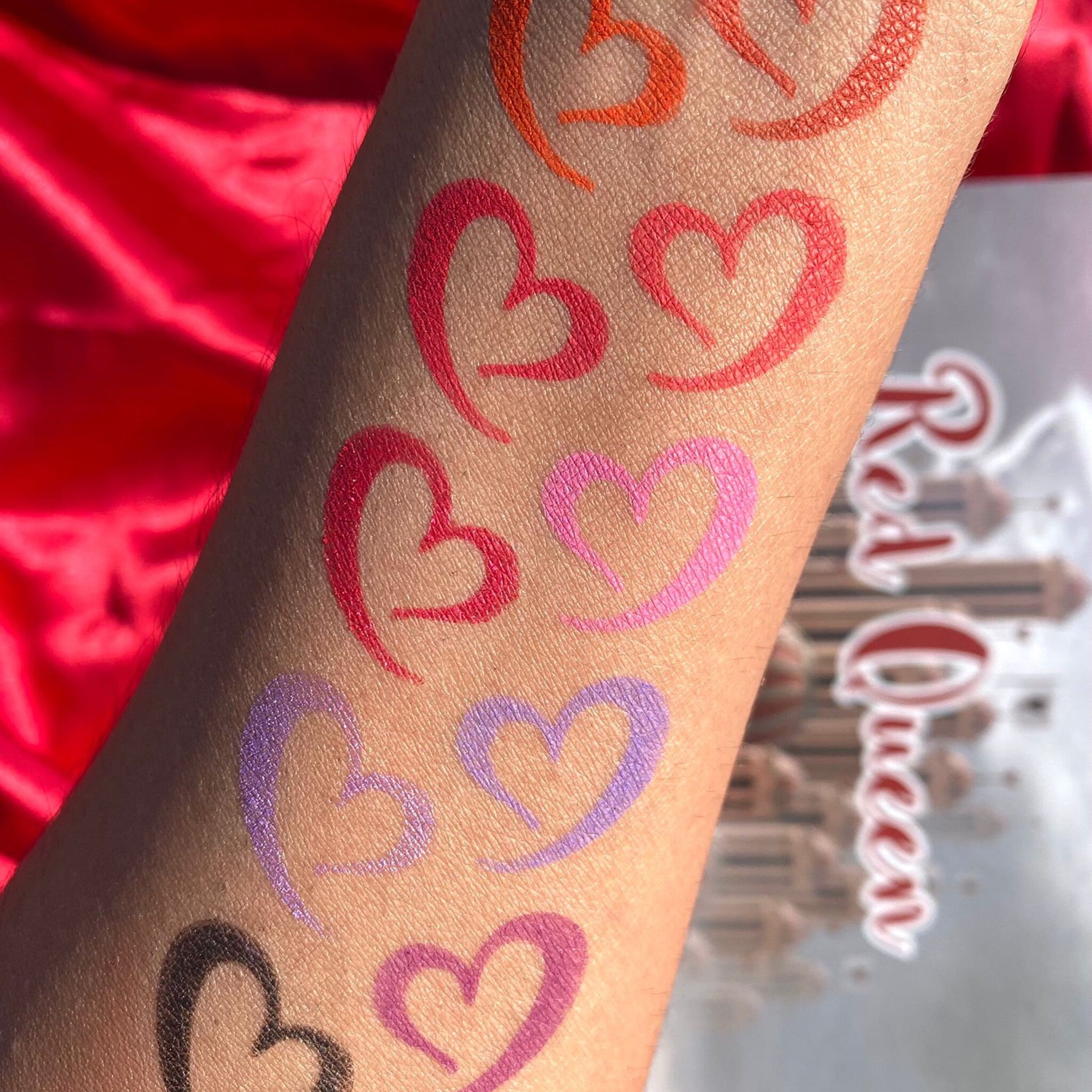 Heart-shaped lip swatches in various colors on arm, with "Red Queen" text visible in background