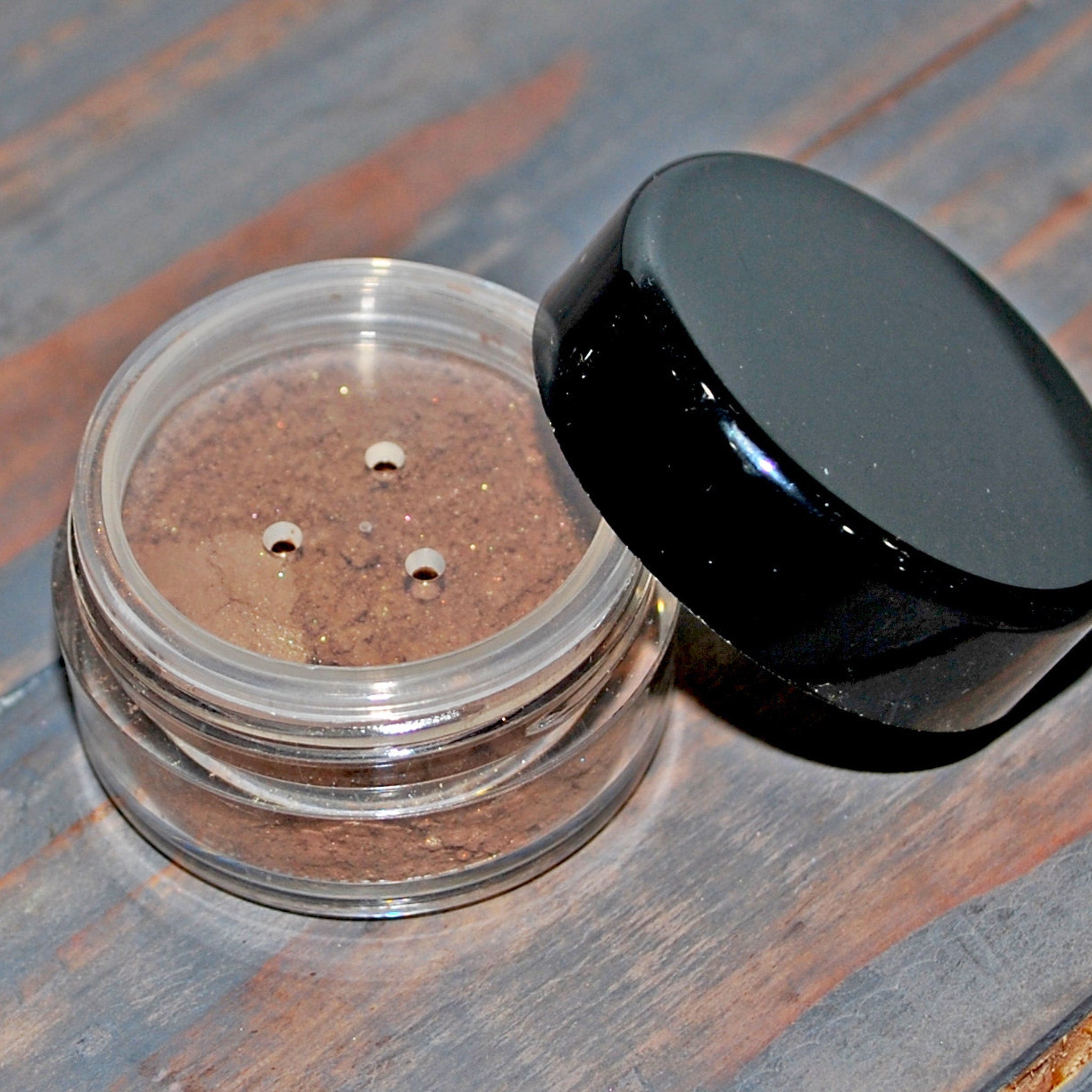 Close-up of fingertips applying shimmering blue and green eye shadow to eyelid with blending brush