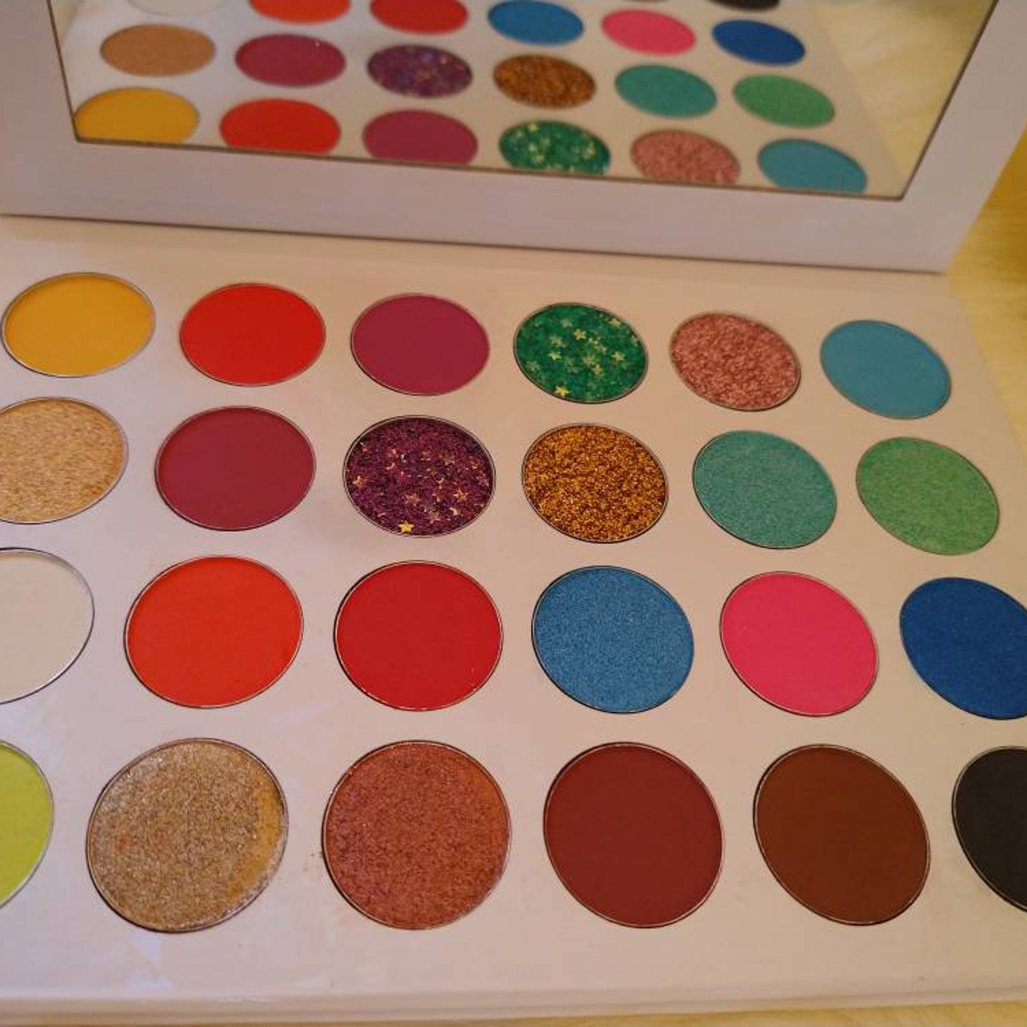 Eyeshadow palette with various colors, including glitter and matte, in a white case