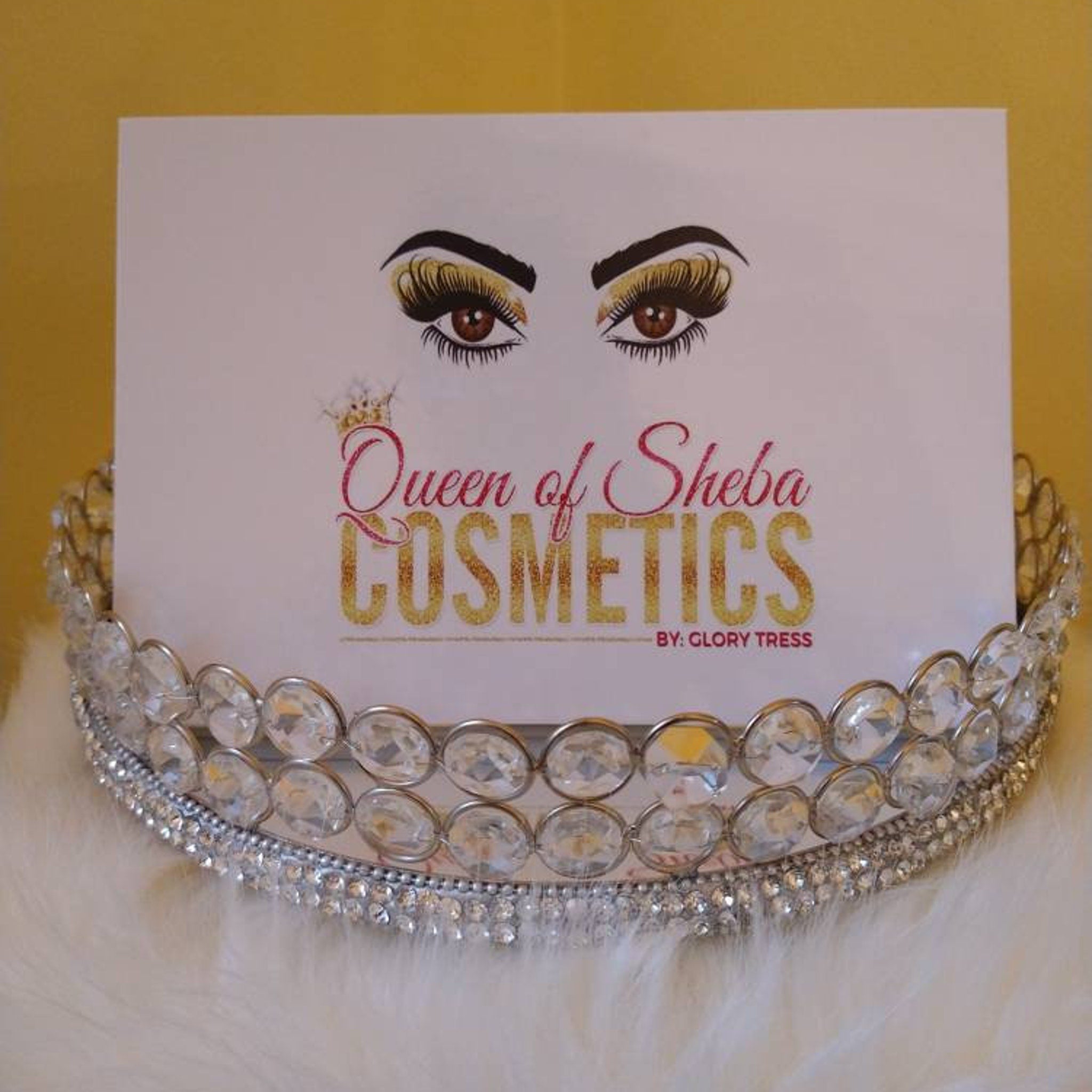 Queen of Sheba Cosmetics logo on white card, with silver rhinestone crown, and white fur background