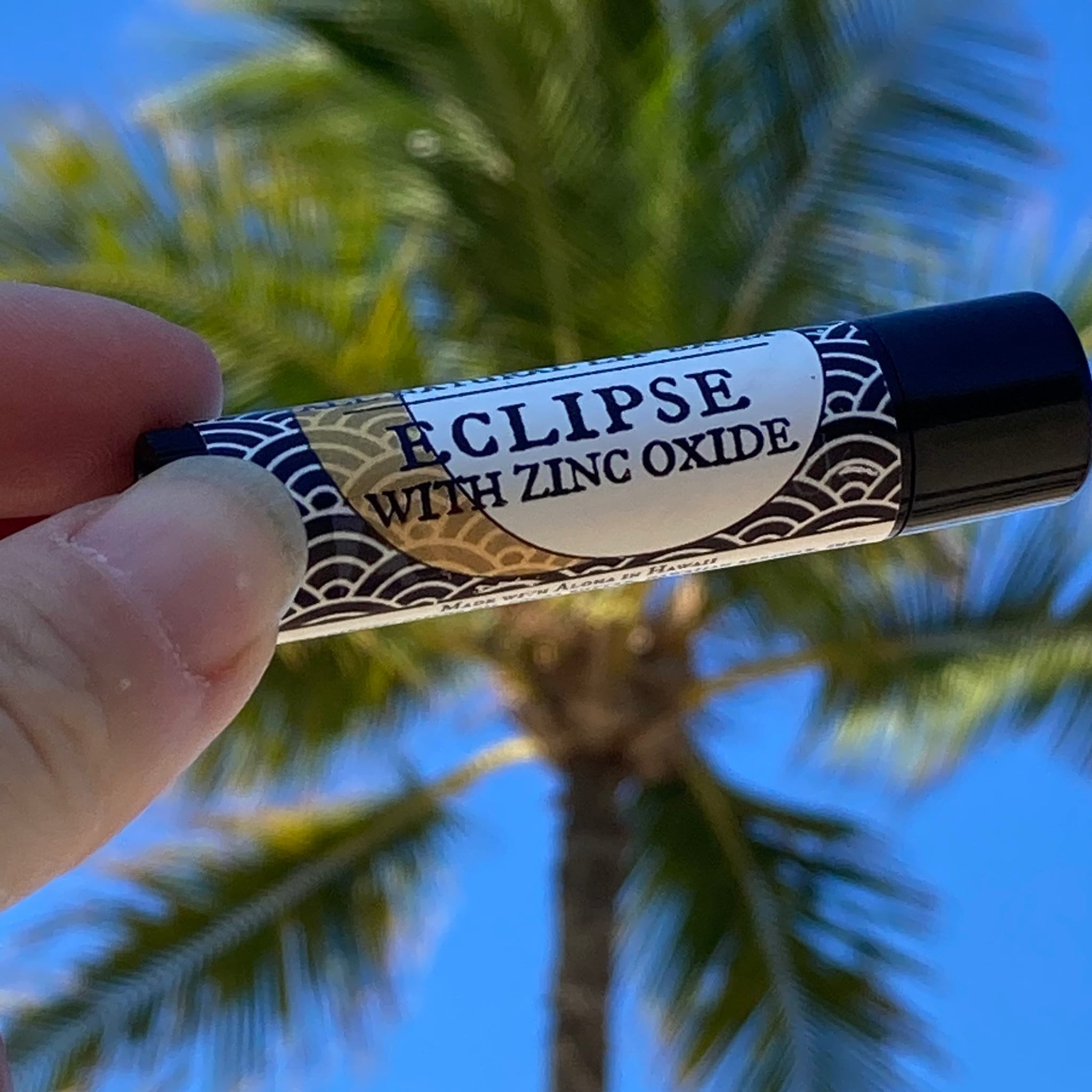 Lip balm with black cap, white label, and wave pattern design, held outdoors