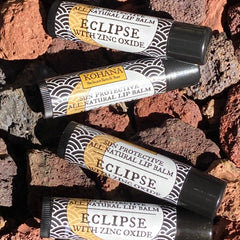 Lip balm tubes with black caps, white and gold labels, and a wave pattern, on red rocks