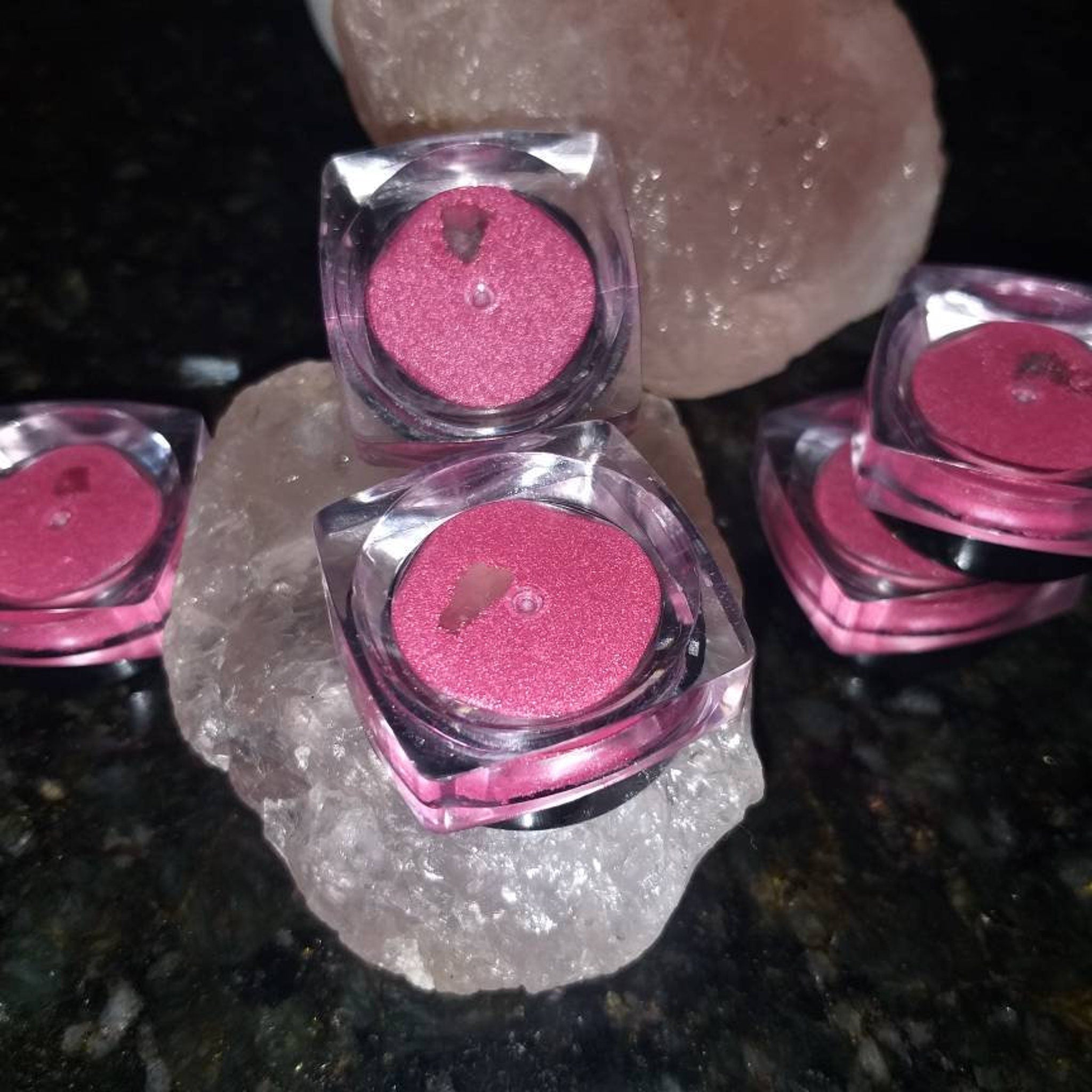 Pink eyeshadow pots in clear plastic containers on a white stone surface
