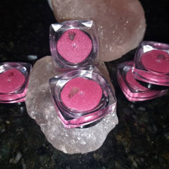 Pink eyeshadow pots in clear plastic containers on a white stone surface