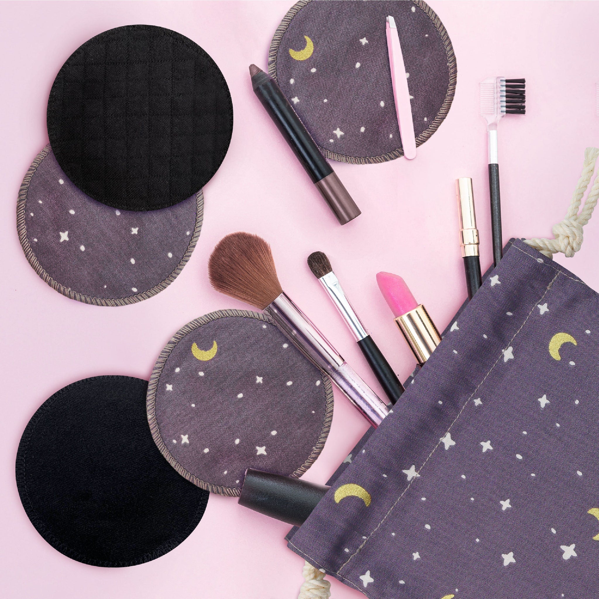 Reusable makeup remover pads, black and patterned fabric, with cosmetic bag and makeup tools on pink surface