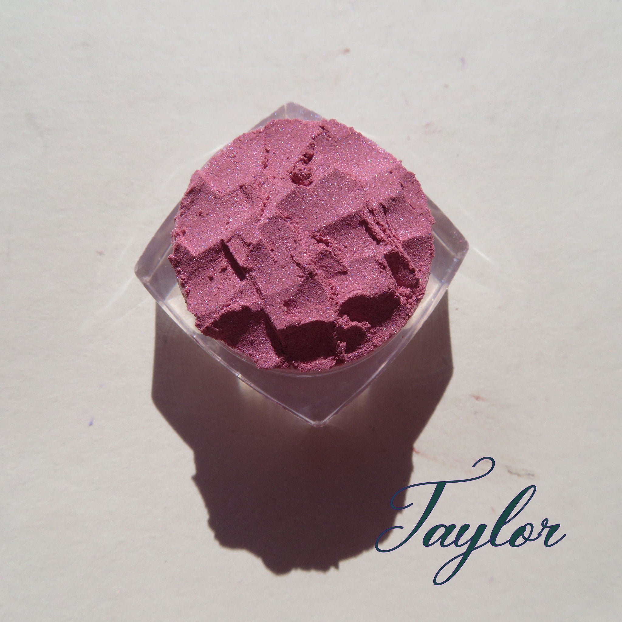Side view of loose mineral eyeshadow in pale pink shimmer, showcasing fine powder texture in glass jar