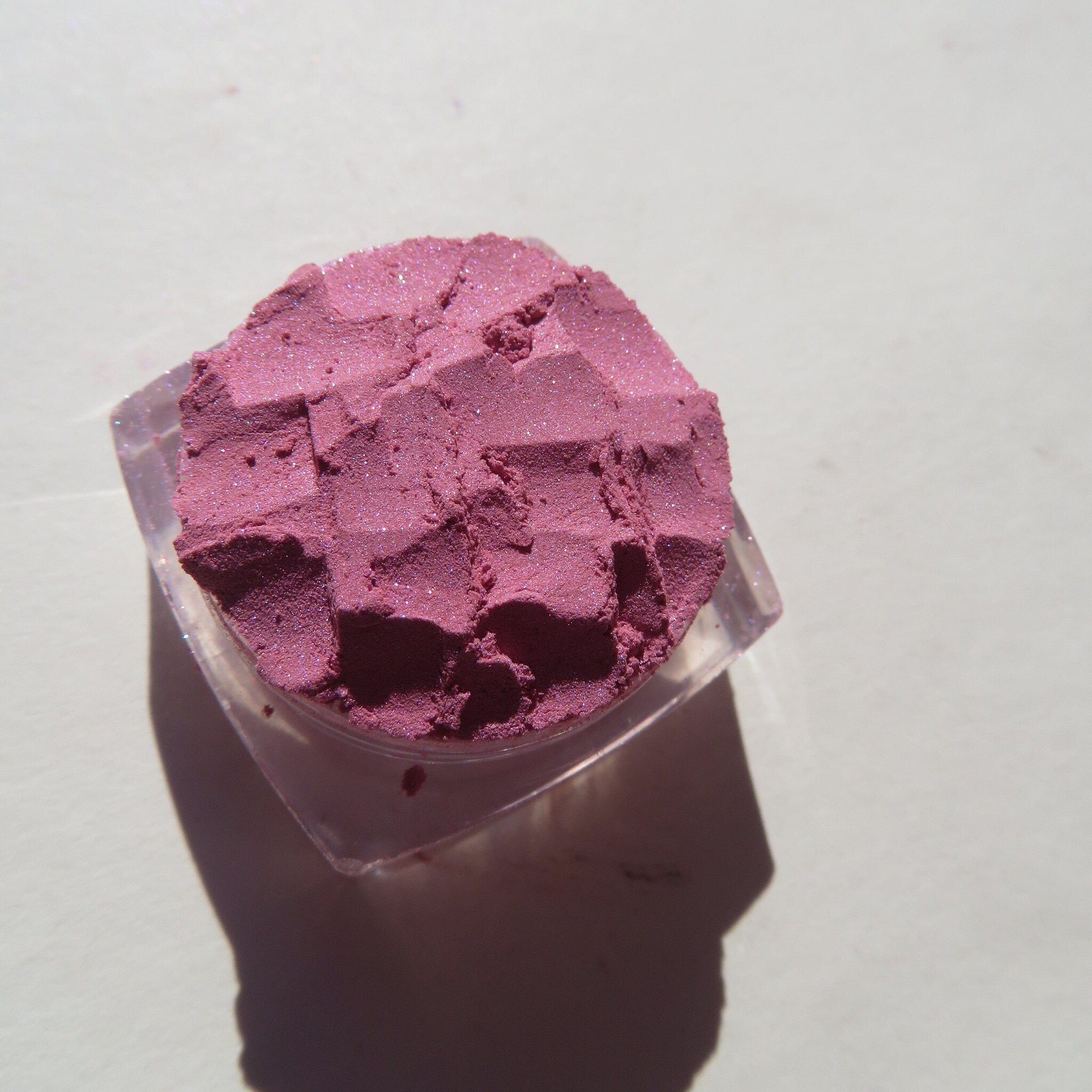 Side view of loose mineral eyeshadow in pale pink shimmer, showcasing fine powder texture in glass jar