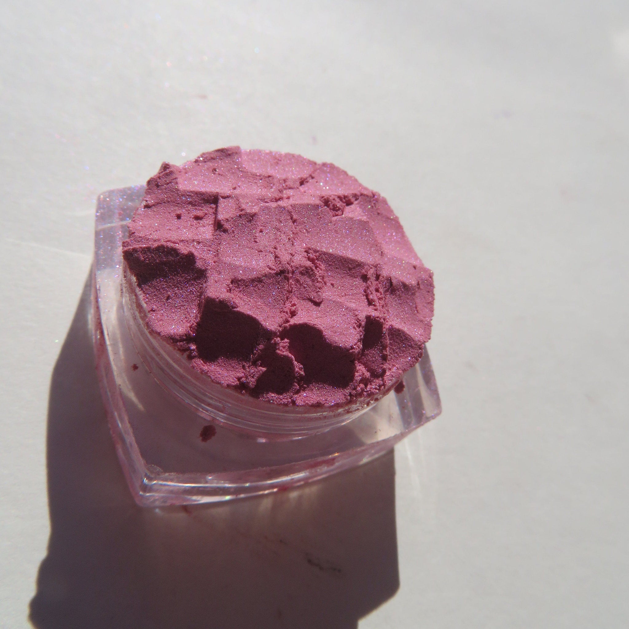 Close-up of loose mineral eyeshadow showing pale pink shimmer particles in natural light
