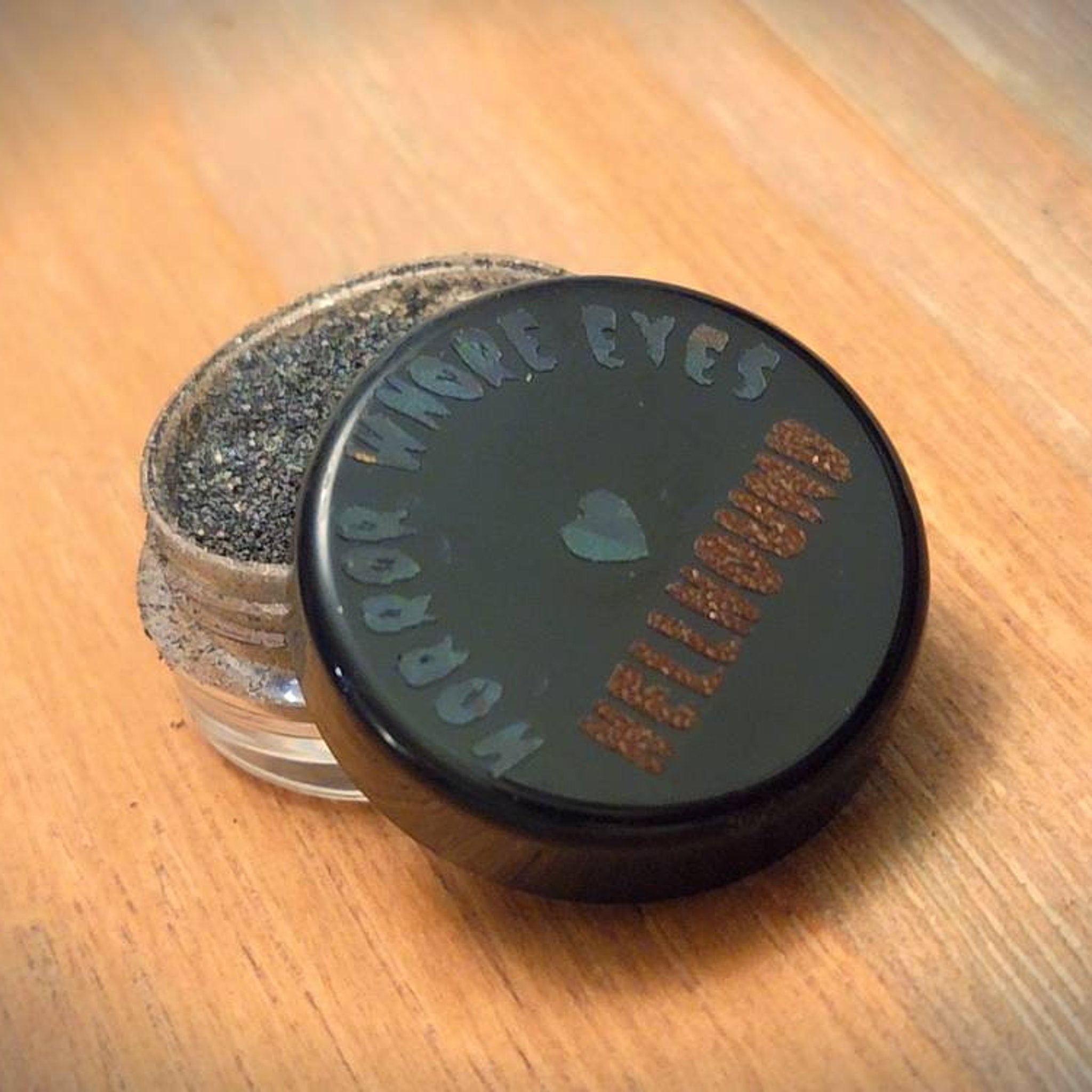 Side view of Hellhound loose eye shadow pigment jar showing shimmering charcoal black powder texture