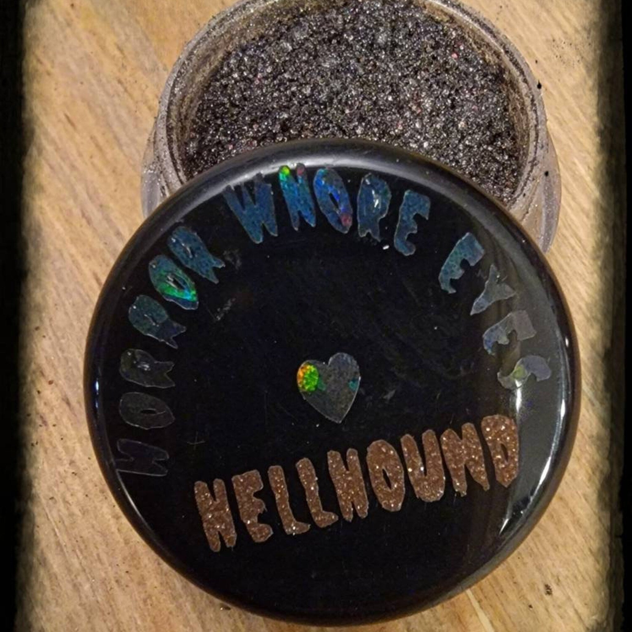 Close-up of Hellhound loose eye shadow pigment jar with black lid and vibrant color visible through clear glass