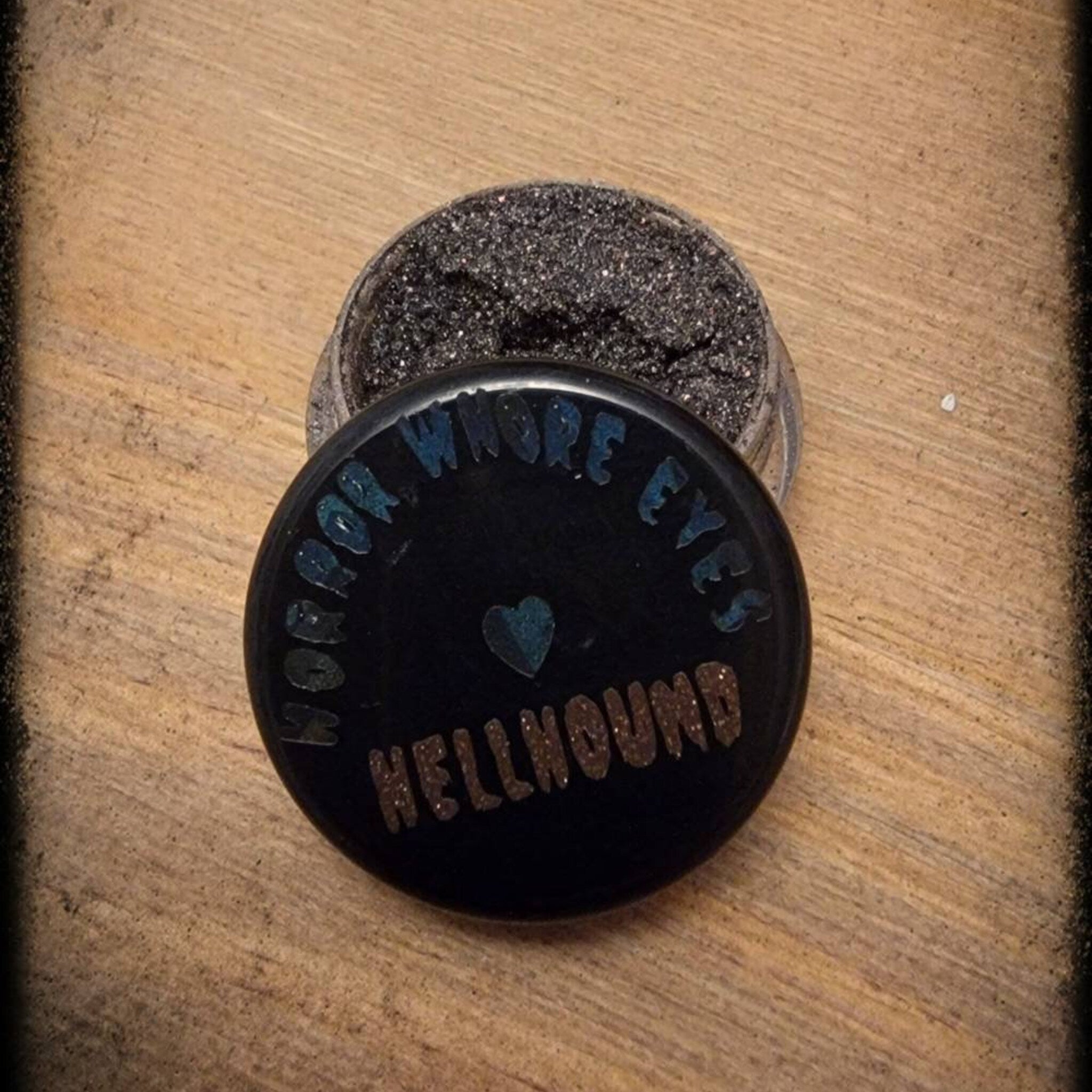 Close-up of Hellhound loose eye shadow pigment showing shimmering charcoal black texture and fine sparkle particles