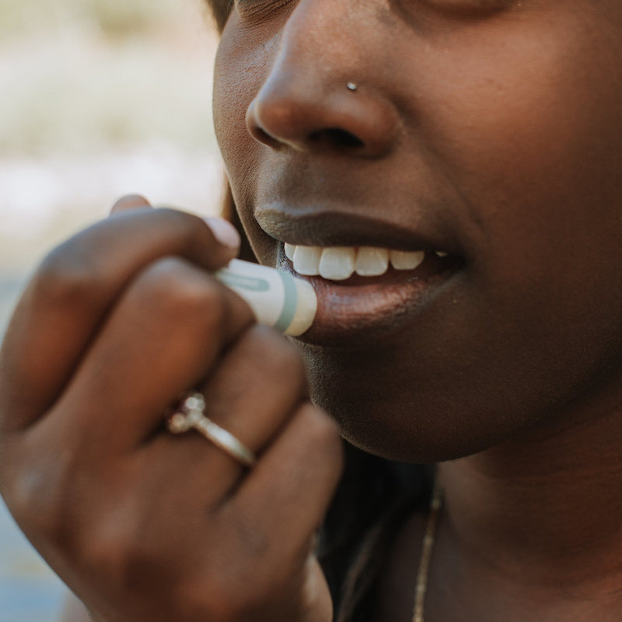 Lip balm tube with white, green accents, and person applying to lips
