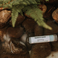 Lip balm tube with white label and text, floating in water with brown rocks and green foliage