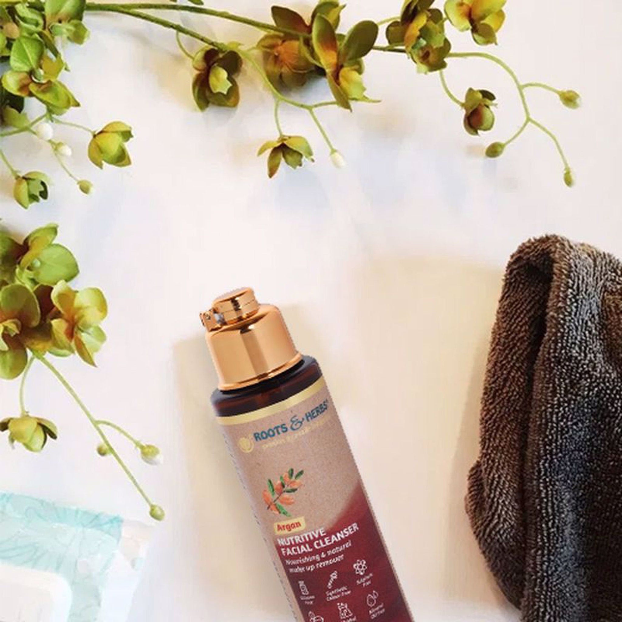 Facial cleanser bottle with gold cap, brown and beige label, and Roots & Herbs brand name visible.